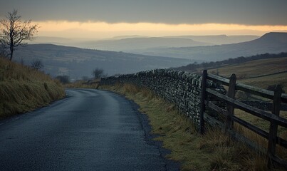 Obraz premium Winding country road at dusk with drystone wall, overlooking misty valley and hills