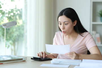 Surprised asian woman calculating expenses at home