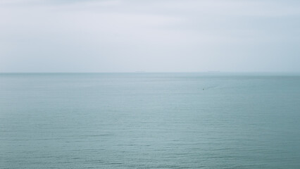 Minimalistic view of a calm sea stretching to the horizon under an overcast sky, with faint ships in the distance