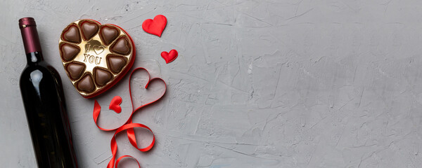 Bottle of red wine on colored background for Valentine Day with gift and chocolate. Heart shaped with gift box of chocolates top view with copy space