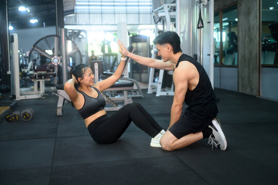 Personal trainer supporting his client during an abdominal workout in the gym