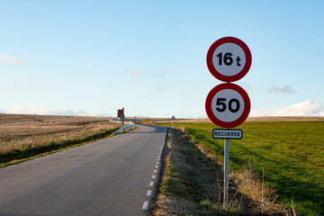 A 50 km h speed limit sign stands next to a rural road, surrounded by crop fields.