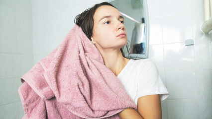 Naklejka premium Young woman wipes hair with towel at bathroom.