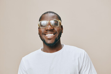 Smiling man wearing stylish glasses and a white T shirt against a neutral beige background, exuding joy and confidence in a modern portrait
