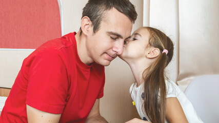 Cheerful small girl daughter and her handsome young dad spending time together at home.
