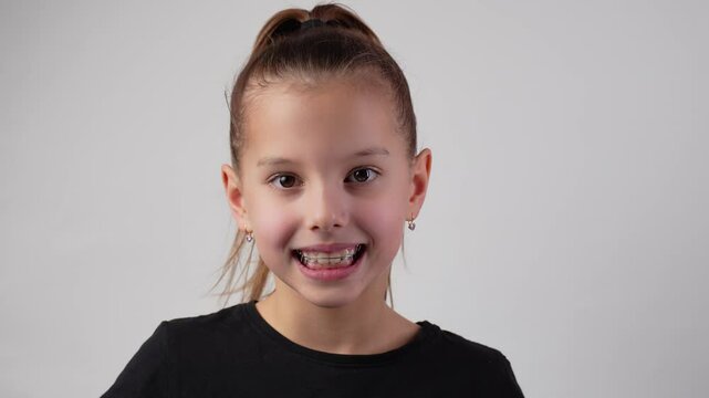 Happy child with dental braces showing thumbs up gesture smiling . Little girl with teeth retainers, smiling, looking at camera, close-up. Child with orthodontic plate on a white background