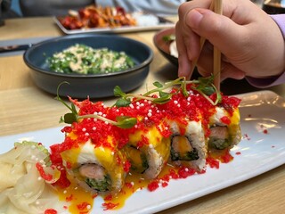 A kids hand hold chopstick take Red Dragon Sushi. Sushi with salmon, panko tiger prawns, cucumber, unagi sauce, mayonnaise, sesame seeds in Japanese restaurant