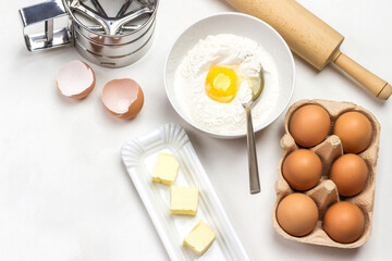 Brown chicken eggs in carton container. Flour, broken egg and spoon in bowl