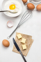Whisk on table. Knife and butter on paper.