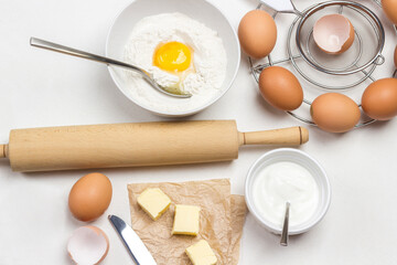 Rolling pin for dough. Broken egg and flour in bowl.