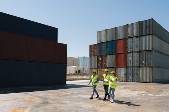 Workers walking together near stack of cargo containers on industrial site