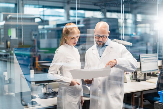 Two technicians wearing lab coats looking at plan