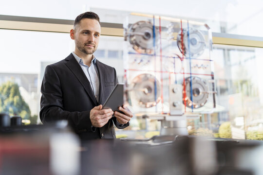 Businessman with tablet looking at machine in a modern factory