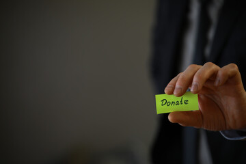 Businessman shows a paper with the word donate. Charitable donation in business concept.