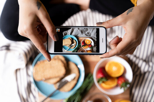 Woman sitting on bed, taking smartphone pictures of her haelthy breakfast