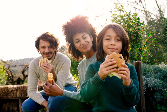 Happy family sitting in garden, taking a break, eating sandwiches