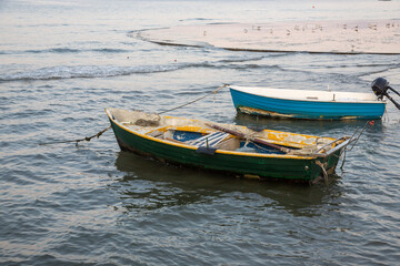 Fototapeta premium Two weathered boats anchored in calm waters during the early morning light near a serene shoreline