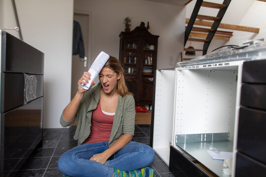 Frustrated young woman with assembly instructions in kitchen