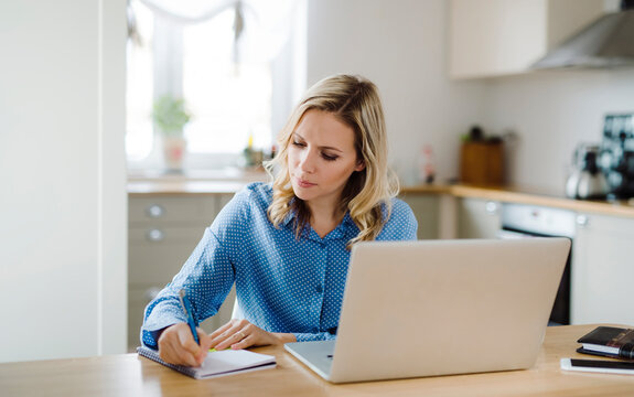 Woman with laptop working at home, taking notes