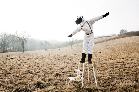 Boy wearing white space suit with raised arms on a step with virtual reality glasses