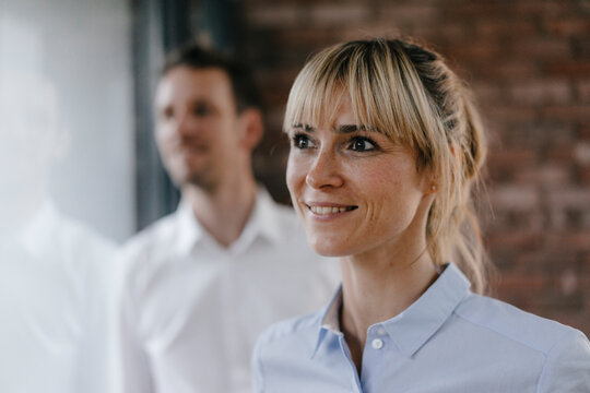 Successful businesswoman and businessman looking out of window, smiling - Powered by Adobe