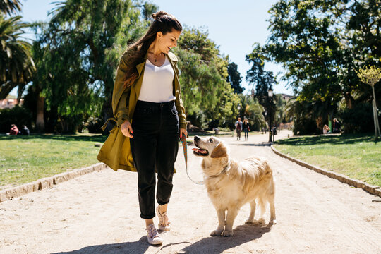 Happy woman going walkies in city park with her Labrador Retriever