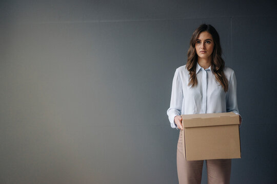 Serious young businesswoman holding cardboard box