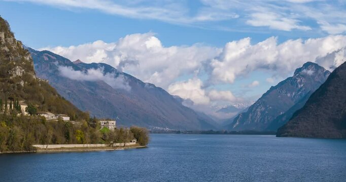 Aerial timelapse view of Lake Idro, an Italian pre alpine lake of glacial origin, reflecting morning light under a blue sky with clouds