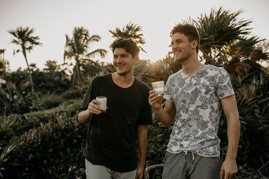 Mexico, Quintana Roo, Tulum, two happy young men having a drink outdoors