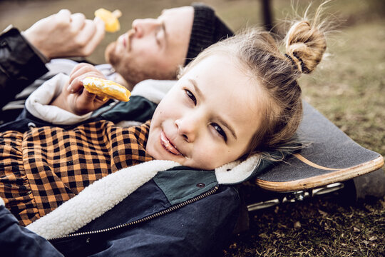 Father and daughter resting on skateboard, eating ice cream