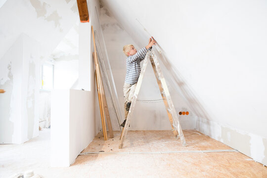 Boy with pocket rule on ladder measuring wall in attic to be renovated