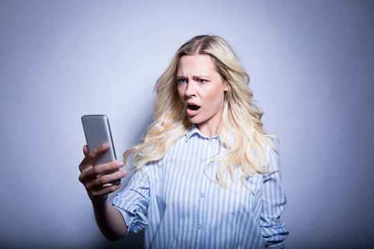 Portrait of disgusted blond woman looking at smartphone