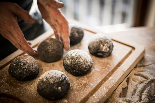 Man preparing black burger buns in kitchen, letting dough rise