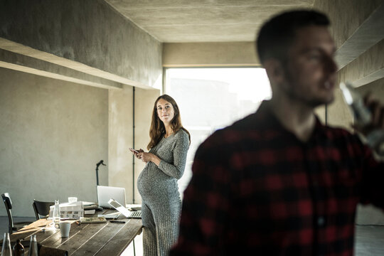 Smiling woman with smartphone watching colleague in office - Powered by Adobe