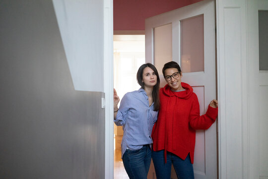 Two girlfriends at home standing in door case, with arms around