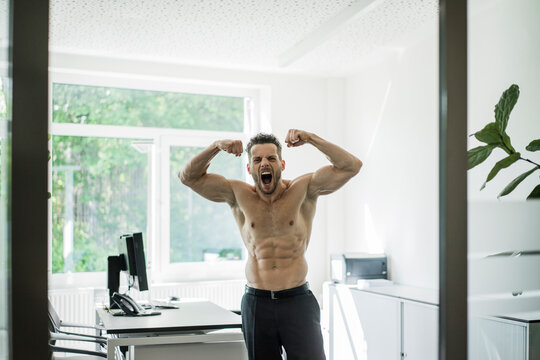 Screaming barechested businessman flexing muscles in office