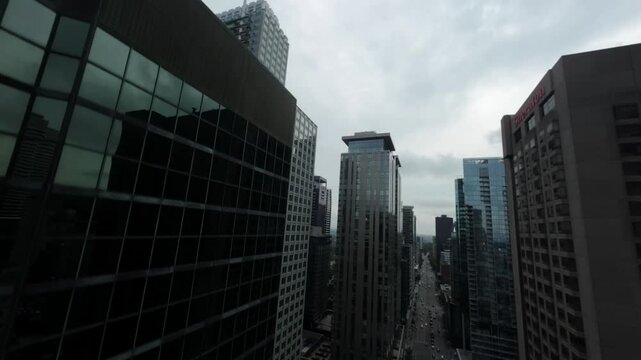 FPV drone flies dynamically along street flanked by tall buildings, then ascends high for stunning aerial view of downtown Montreal at Square Dorchester.