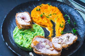 Chicken Cordon Bleu with carrot puree and spinach mashed potatoes on a black board close-up. A traditional French dish in an original presentation. Healthy eating and diet concept.