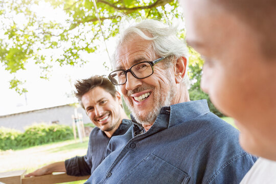 Men of a family sitting on a swing bed ing the garden, talking