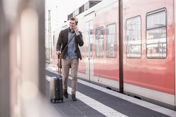 Smiling young man on cell phone walking on station platform along commuter train