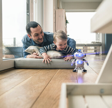 Excited father and son lying on a mattress at home watching a toy robot