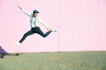 Young man in front of pink construction barrier, jumping in the air