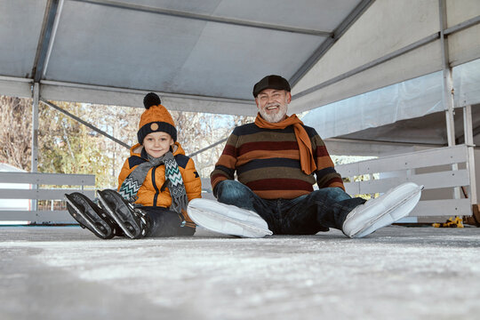 Grandfather and grandson on the ice rink, sitting on ice