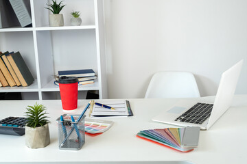 Designer  workplace laptop color sampler catalog empty notepad pen and coffee at office desk