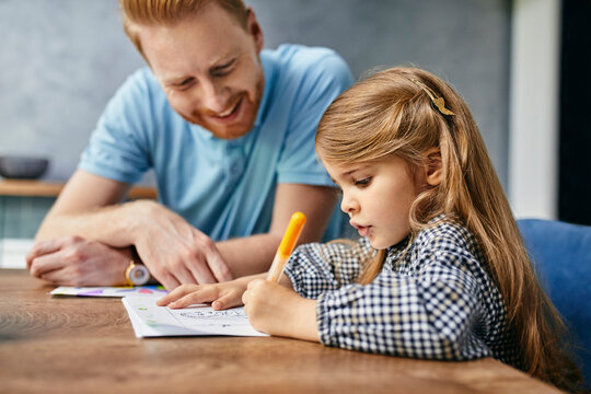 Father and daughter sitting at table, painting colouring book