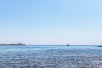 A tranquil scene of a sailboat gliding across the crystal-clear waters of the Aegean Sea, with a small island in the distance