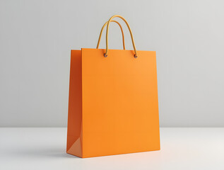 Bright orange shopping bag with gold handles on light grey background is a versatile template for showcasing branding or product design. Stylish and minimalistic look.