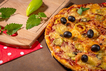 Pepperoni, black olives, and mozzarella pizza on a wooden cutting board with green pepper