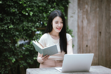 Obraz premium A confident young Asian woman is working on her laptop in a vibrant park. E-banking and career aspirations in a modern lifestyle.