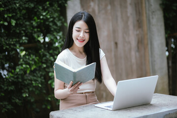 Obraz premium A confident young Asian woman is working on her laptop in a vibrant park. E-banking and career aspirations in a modern lifestyle.